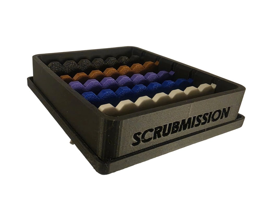 A 3D-printed Scrubmission storage tray holding rows of textured scrub balls in black, brown, purple, blue, and white, on a neutral light gray background.