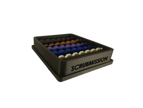 A 3D-printed Scrubmission storage tray holding rows of textured scrub balls in black, brown, purple, blue, and white, on a neutral light gray background.